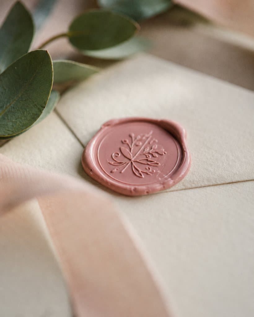 A blush wax seal pressed into a cream wedding envelope